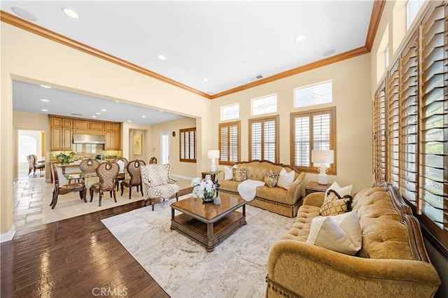 living room featuring baseboards, ornamental molding, recessed lighting, a high ceiling, and wood-type flooring