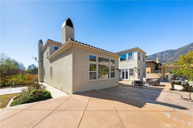 back of property with stucco siding, a patio, fence, a mountain view, and a chimney