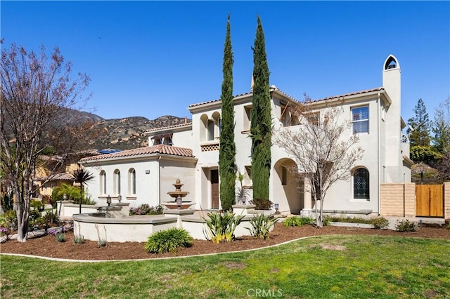 back of house with fence, stucco siding, a chimney, a tile roof, and a lawn