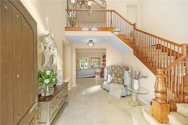 foyer with stairway, baseboards, a notable chandelier, and a towering ceiling