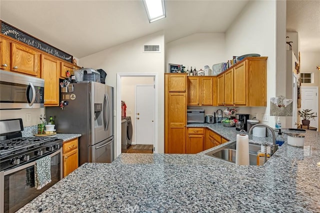 kitchen with lofted ceiling, stainless steel appliances, a sink, light stone countertops, and washer / clothes dryer