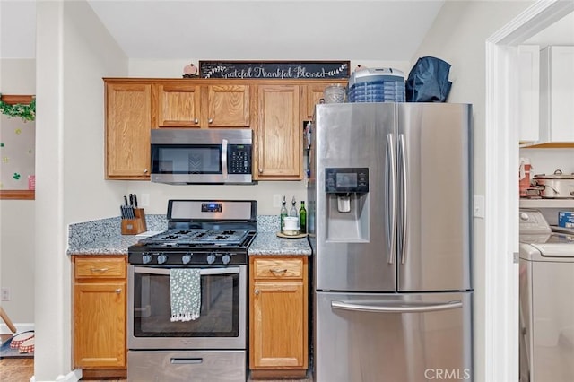 kitchen featuring appliances with stainless steel finishes, washing machine and dryer, and light stone countertops