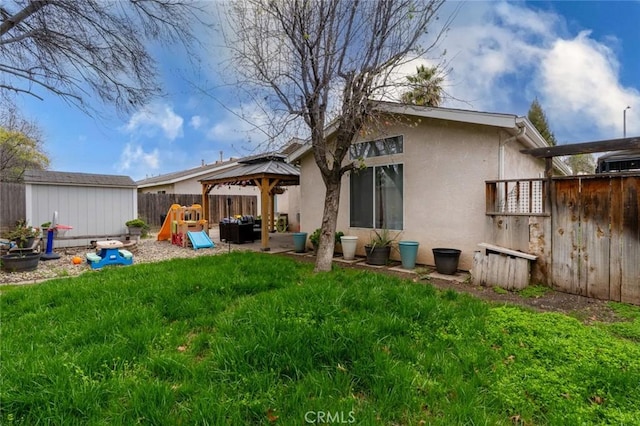 back of house featuring a storage unit, stucco siding, a gazebo, a fenced backyard, and an outdoor structure