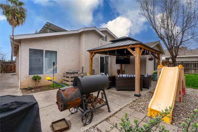 rear view of property featuring an outdoor hangout area, fence, a gazebo, a patio area, and stucco siding