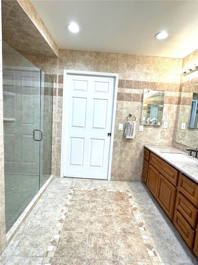 bathroom with recessed lighting, a shower stall, tile walls, and vanity