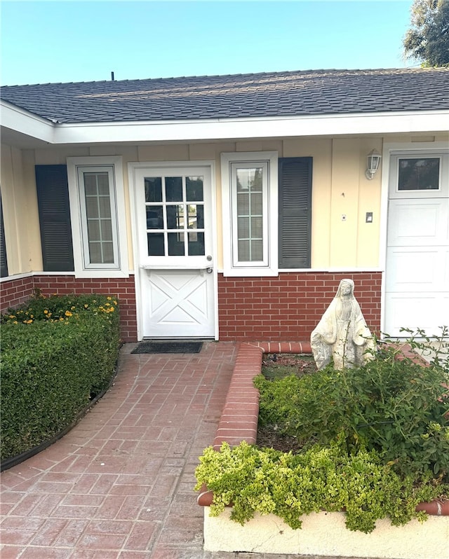 view of exterior entry featuring roof with shingles and brick siding