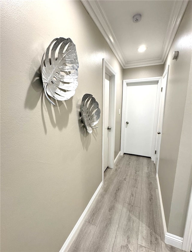 hallway featuring baseboards, ornamental molding, and light wood-style floors