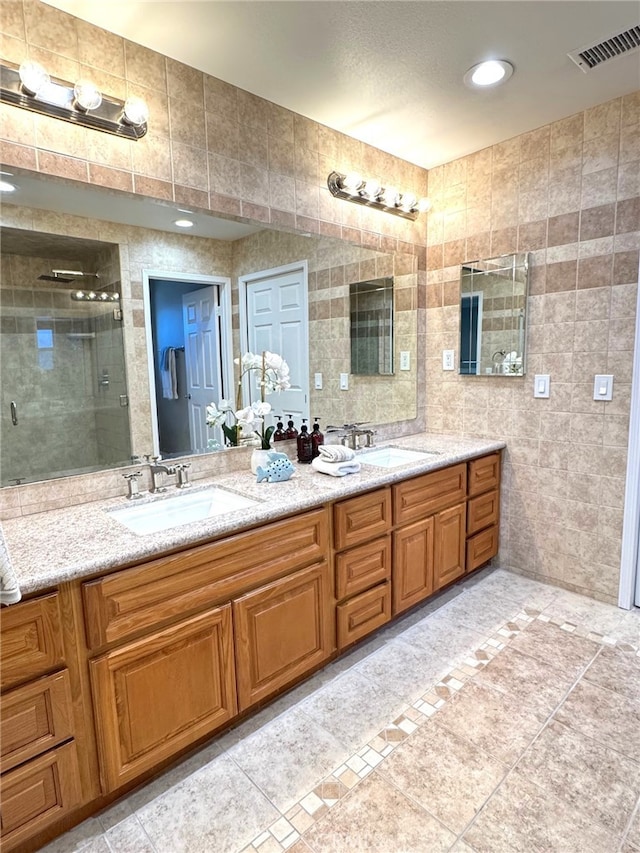 bathroom featuring a stall shower, visible vents, a sink, and tile walls