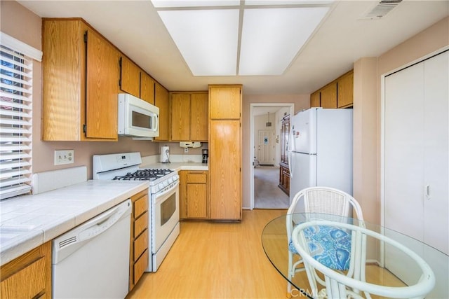 kitchen with light wood-style flooring, white appliances, visible vents, tile counters, and brown cabinets