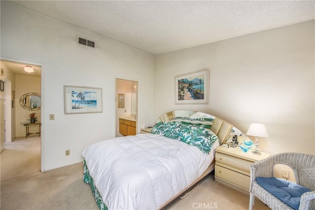 bedroom featuring visible vents, ensuite bathroom, a textured ceiling, and light colored carpet