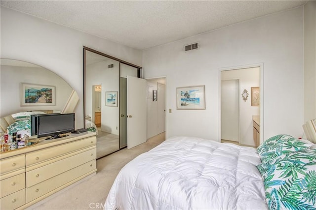 bedroom featuring light carpet, a textured ceiling, ensuite bath, and visible vents