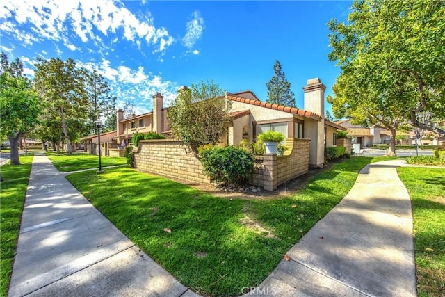 view of side of home featuring stucco siding, a tile roof, a chimney, and a yard