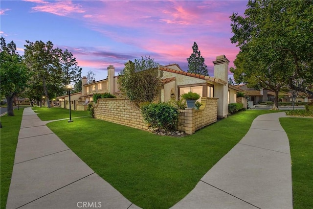 property exterior at dusk featuring a tiled roof, a lawn, a chimney, and stucco siding