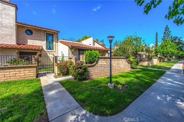 exterior space featuring stucco siding, a tile roof, a gate, fence, and a front yard