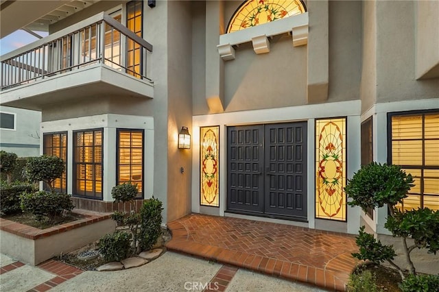 view of exterior entry featuring a balcony and stucco siding