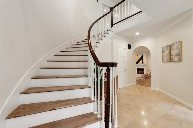 stairs with a warm lit fireplace, baseboards, ornamental molding, a high ceiling, and recessed lighting