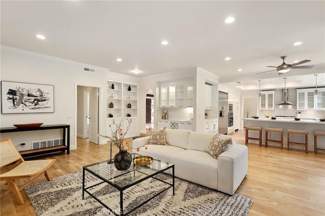 living room with visible vents, arched walkways, light wood-style flooring, crown molding, and recessed lighting