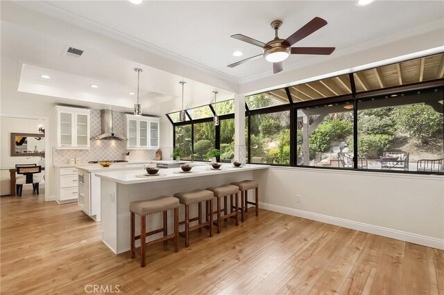 kitchen featuring light wood finished floors, visible vents, glass insert cabinets, white cabinetry, and wall chimney exhaust hood