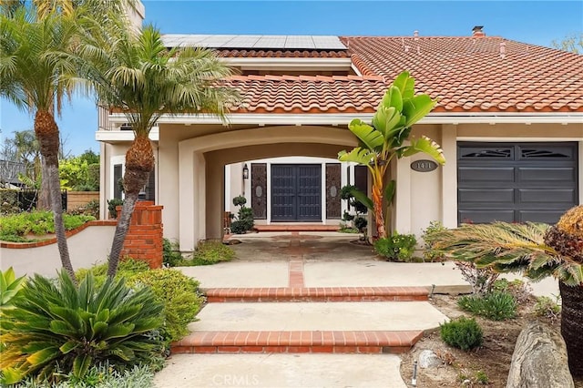 entrance to property featuring a garage, a tiled roof, roof mounted solar panels, and stucco siding