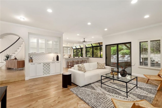 living room with ornamental molding, arched walkways, light wood-style flooring, and recessed lighting