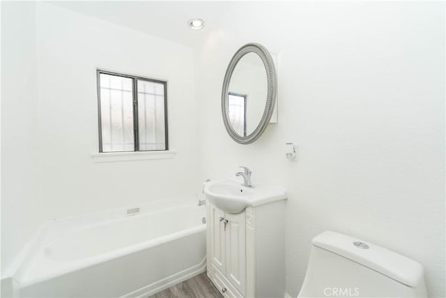 full bath featuring wood finished floors, toilet, vanity, and a bath