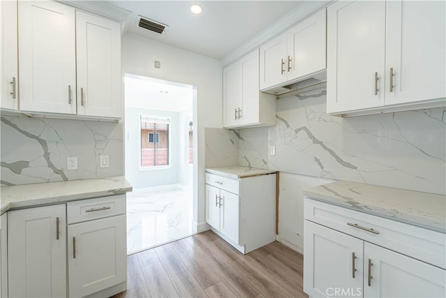 kitchen with light stone counters, tasteful backsplash, visible vents, white cabinets, and light wood-style floors