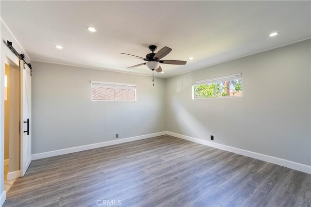 unfurnished room featuring baseboards, a barn door, wood finished floors, and recessed lighting