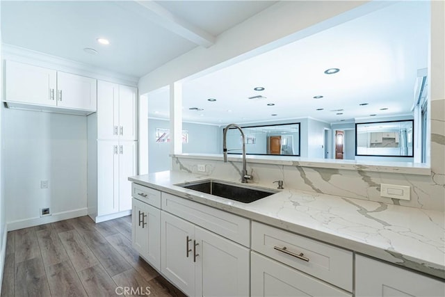 kitchen with white cabinetry, backsplash, a sink, light wood-style flooring, and light stone countertops