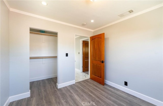 unfurnished bedroom with crown molding, baseboards, visible vents, a closet, and wood finished floors