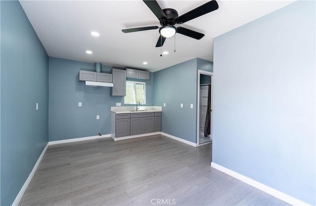 kitchen with a sink, baseboards, gray cabinetry, and light wood-type flooring