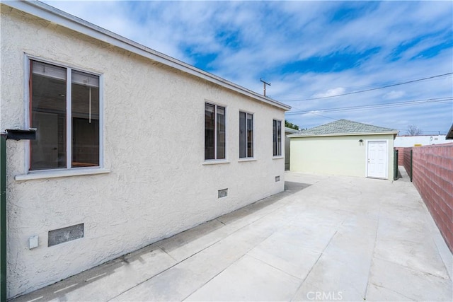 view of property exterior featuring fence, a patio, crawl space, stucco siding, and an outdoor structure