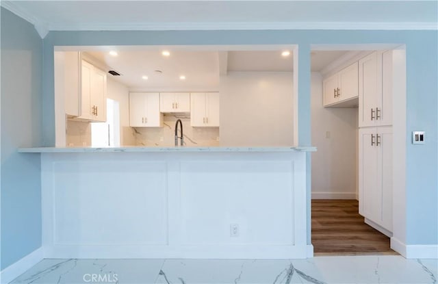 kitchen with a peninsula, marble finish floor, tasteful backsplash, white cabinetry, and a sink