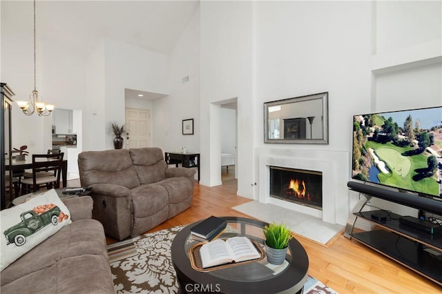 living room featuring a glass covered fireplace, wood finished floors, a towering ceiling, and a notable chandelier