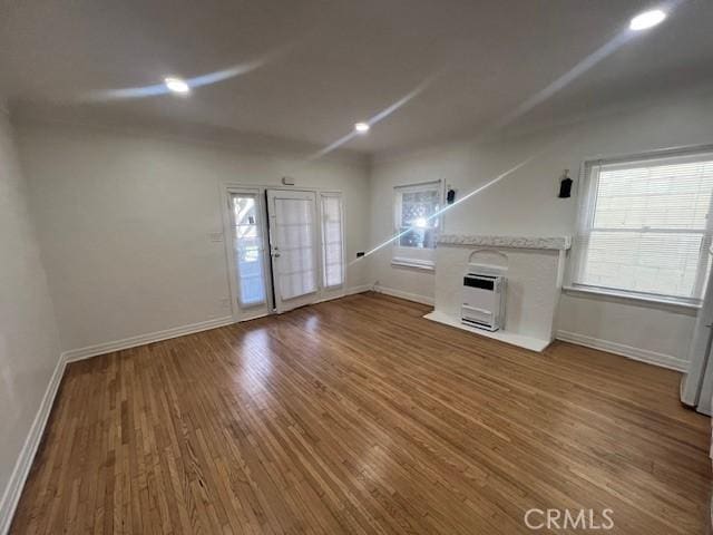 unfurnished living room with recessed lighting, heating unit, wood finished floors, and baseboards