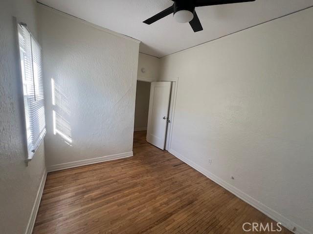 unfurnished room with a textured wall, a ceiling fan, baseboards, and wood finished floors