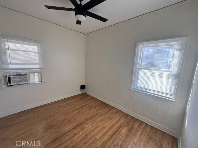 empty room featuring cooling unit, baseboards, wood finished floors, and a ceiling fan