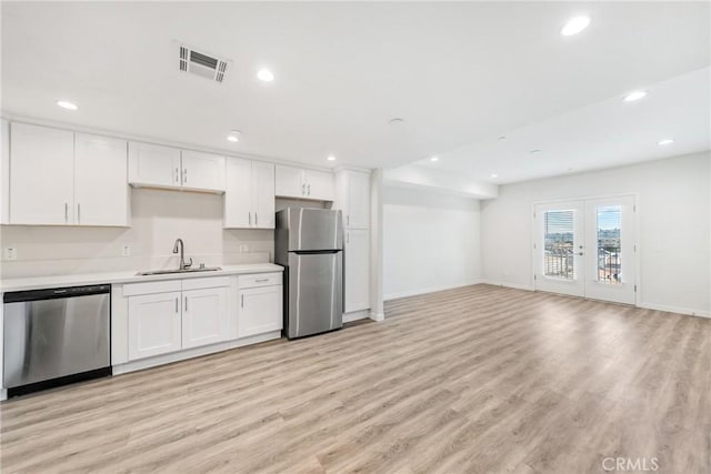 kitchen featuring visible vents, white cabinets, stainless steel appliances, light wood-style floors, and a sink