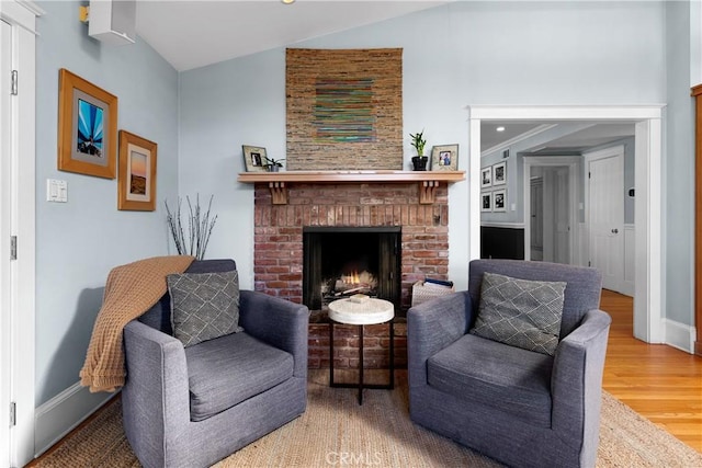 sitting room with lofted ceiling, a brick fireplace, baseboards, and wood finished floors