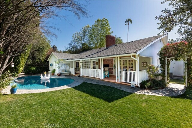 rear view of house with a chimney, a yard, and an outdoor pool