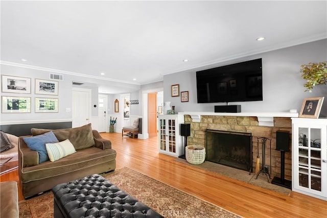 living area with a fireplace, wood finished floors, visible vents, and crown molding