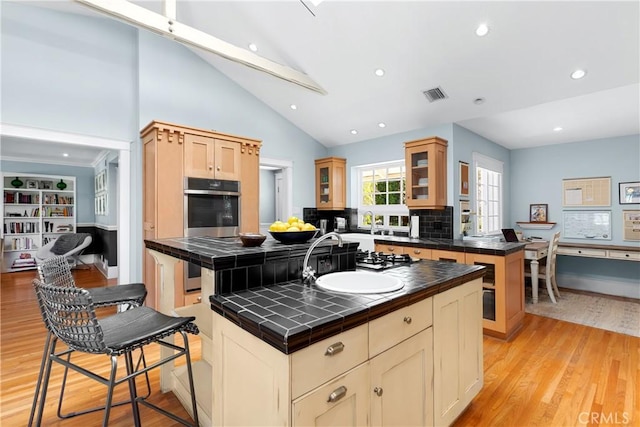 kitchen featuring tile countertops, a sink, visible vents, light wood finished floors, and glass insert cabinets