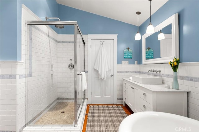 bathroom with a wainscoted wall, tile walls, lofted ceiling, a stall shower, and vanity