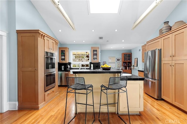 kitchen with glass insert cabinets, a kitchen bar, a center island, vaulted ceiling, and stainless steel appliances