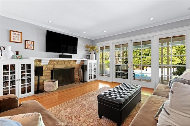 living room with crown molding, a stone fireplace, and wood finished floors