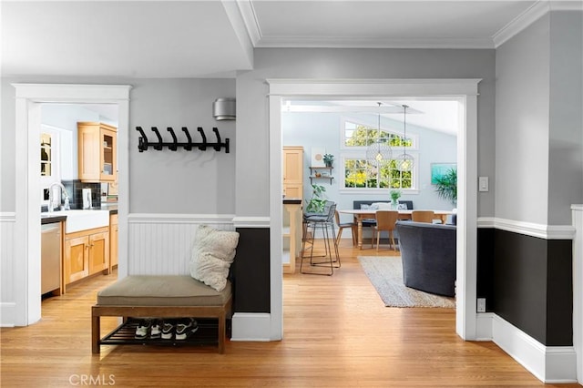 interior space featuring crown molding, wainscoting, vaulted ceiling, a sink, and light wood-type flooring