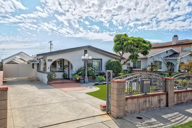 view of front of property featuring driveway, a fenced front yard, covered porch, a gate, and stucco siding