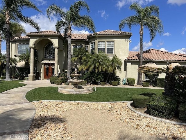 mediterranean / spanish-style house featuring a tiled roof, a front yard, and stucco siding