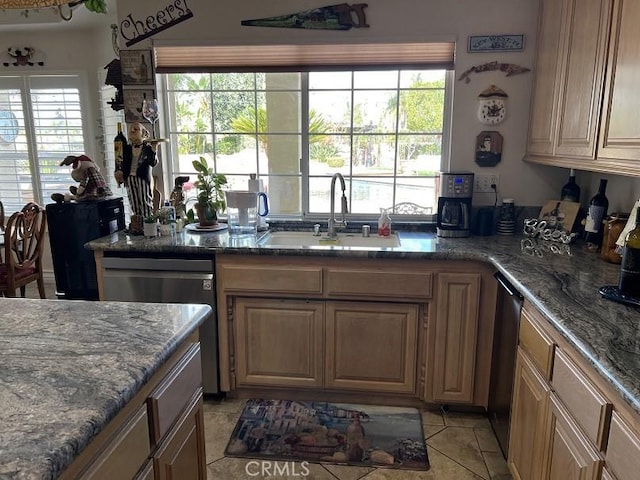 kitchen featuring dishwasher, dark stone counters, light tile patterned flooring, and a sink