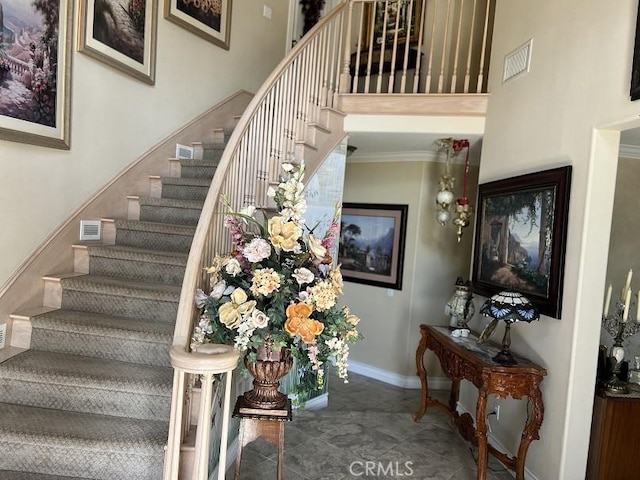 stairway with a towering ceiling, baseboards, visible vents, and ornamental molding