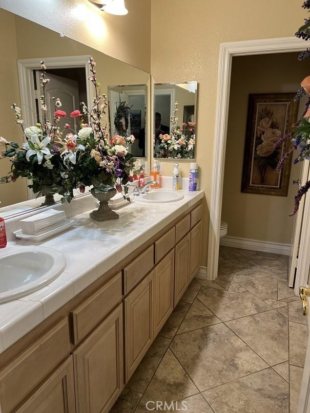 full bathroom featuring baseboards, a sink, toilet, and double vanity